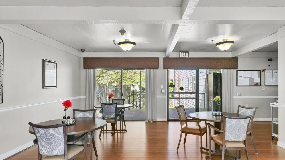 A dining room with round wooden tables, chairs with patterned backs, and large windows leading to an outdoor patio