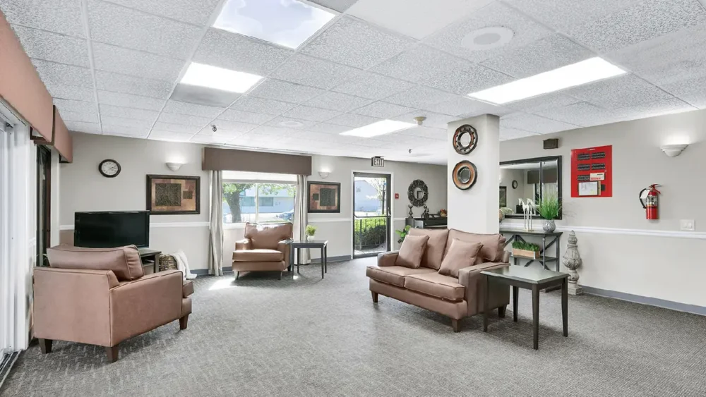 A living room with gray carpet, two brown armchairs, a brown couch, and a mirror on the wall